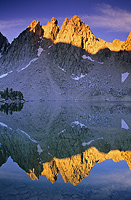 Kearsarge peaks and spires in the Sierra Nevada Mountains reflecting in a lake as the sun rises to light  the top of the peaks 
