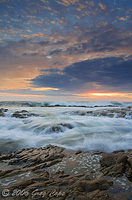 Waves crashing and the sun setting over tidepools and a beautiful sky