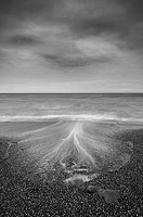 Black and white long exposure of waves on a pebble beach with storm clouds overhead