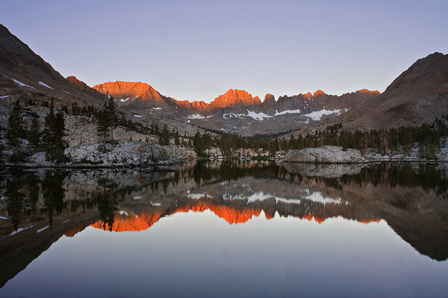 Glowing sunrise hitting alpine and metamorphic Kaweah Peaks as they tower over a basin in summer reflecting in a lake