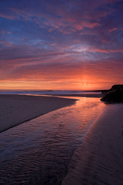 Dramatic sunset colors glowing across the sky and stream on the sandy beach