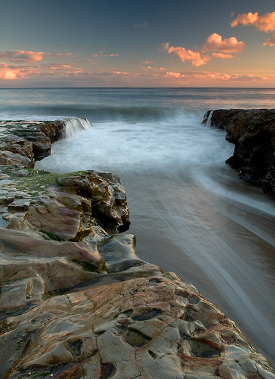 Water rushing past the rocks as the sun sets along the horizon.