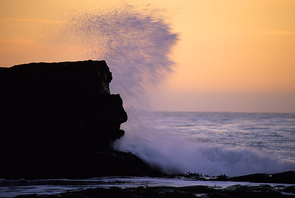 Waves crashing off rocks with the dusk sky in the background