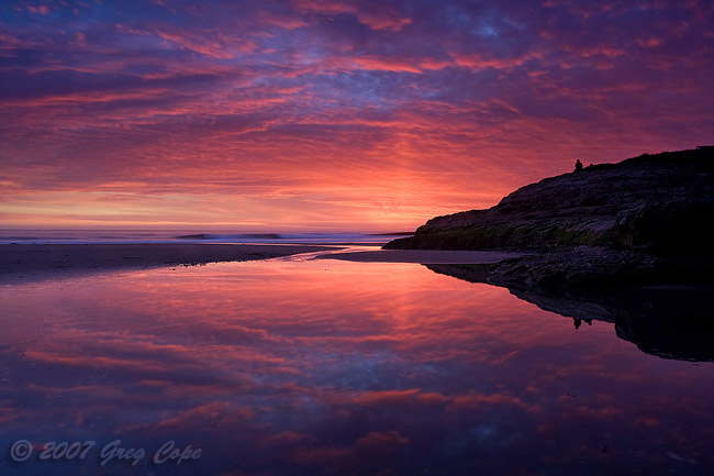 Dramatic sunset colors glowing off clouds and reflecting in water along the beach