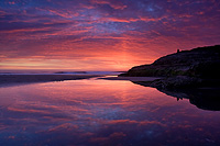 Dramatic sunset colors glowing off clouds and reflecting in water along the beach