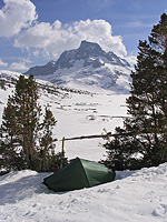 A tent placed in the snow with a backdrop of snow and ice and large mountains 