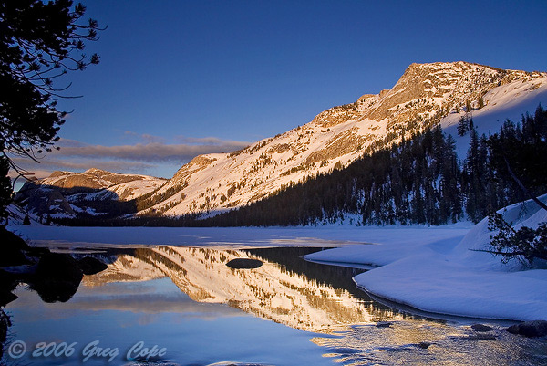 Frozen Tenaya Lake in winter as the sun sets and alpenglow light hit the mountains of the high country of Yosemite