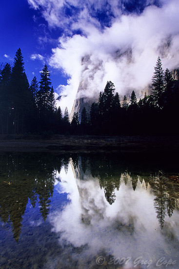 El Capitan and trees reflecting in a river while being surrounded by blue sky and clouds